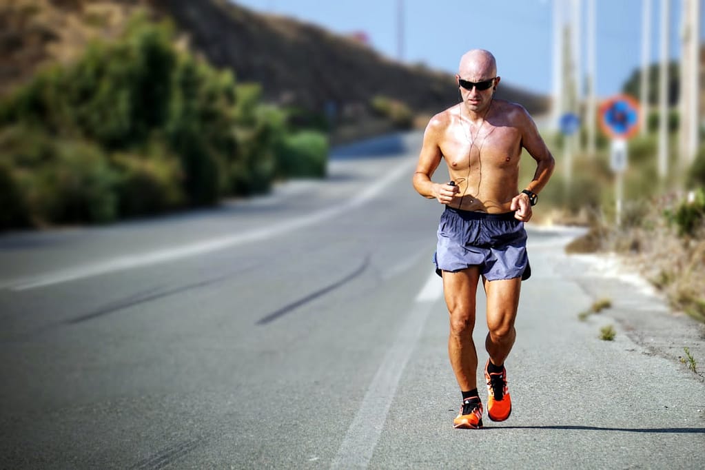 Middle-aged man running on a sunny day, on a hot paved road, illustrating the effects of exercise on metabolism and epigenetics.