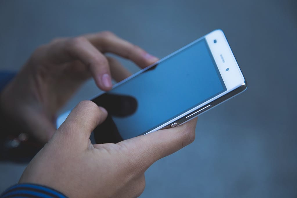 Close-up of teenage girl’s hands, scrolling on her phone, symbolising social media use and societal pressures.