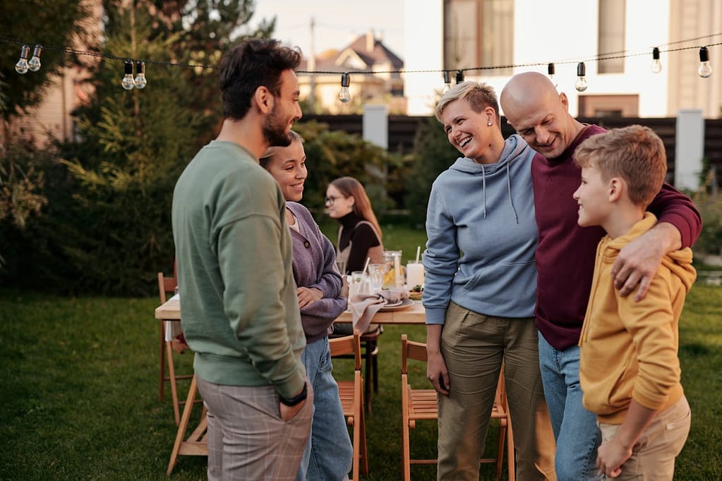 A family gathering outdoors in a garden, with some members standing and talking while others are sitting and eating, representing the fluidity of identity in social settings.