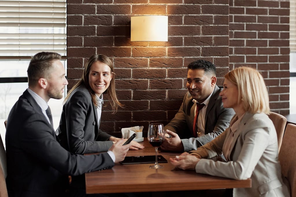 Four successful friends in business attire, sitting together at a table, enjoying a lively conversation.