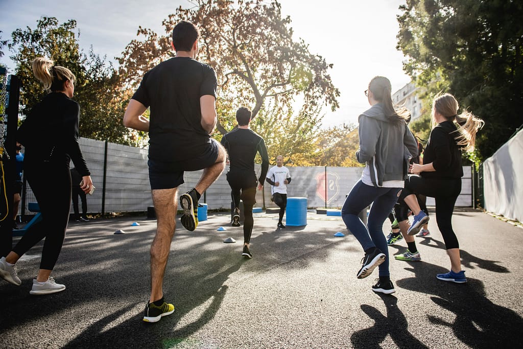 A group of people exercising outdoors in the sunshine, performing knee lifts together in a bright and energetic setting.