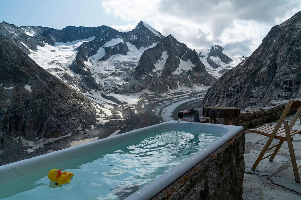 A bath tub filled with water, set in the snowy mountains, with a rubber duck floating on the water.