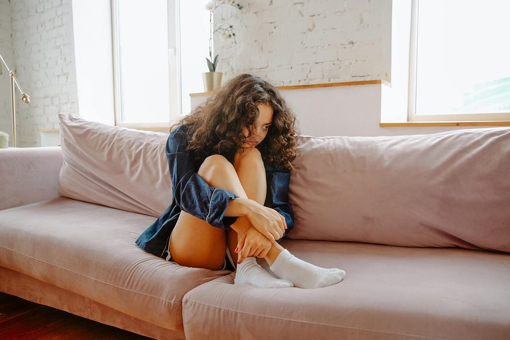 Girl sitting on the sofa curled up with knees at her chest.