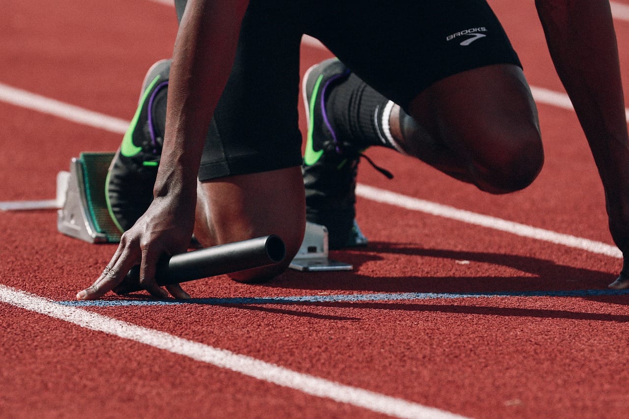 Elite sprinter in starting position on relay track, demonstrating high performer discipline