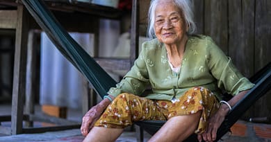 A centenarian woman sitting in a hammock, smiling warmly.