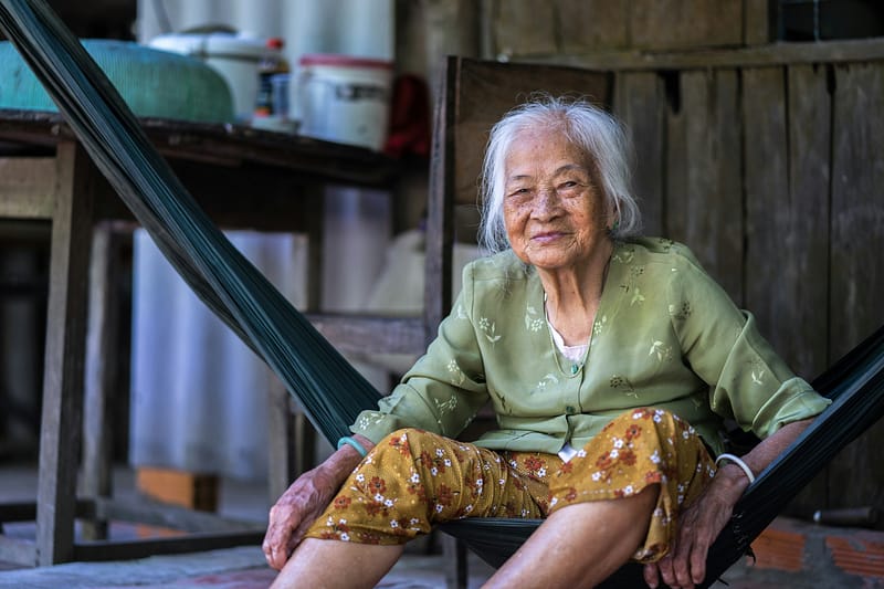 A centenarian woman sitting in a hammock, smiling warmly.