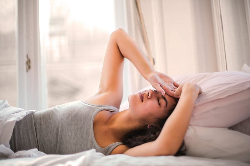 Woman lying in bed with a headache, holding her head in discomfort.