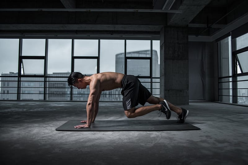 Fit man doing plank knee crunches in an empty industrial building under spotlight, symbolizing focus and discipline.