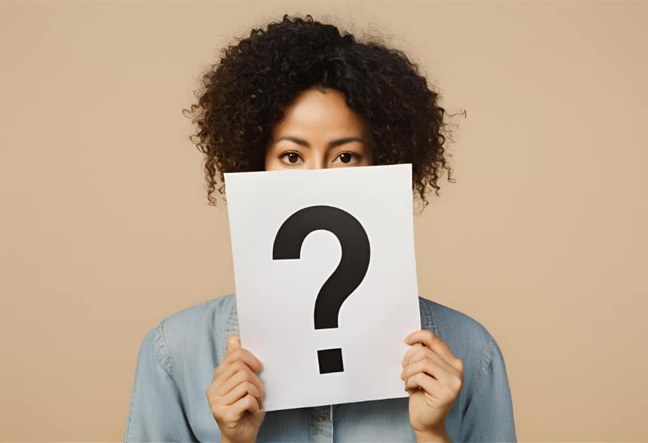 A person stands in the center of a plain background, holding a large piece of paper with a question mark printed on it, obscuring their face. The image symbolizes uncertainty and exploration of one's identity.